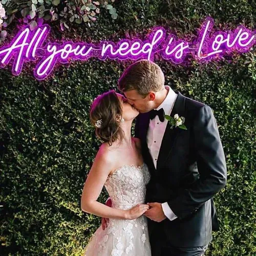 Pink LED neon sign reading All You Need Is Love behind a couple
